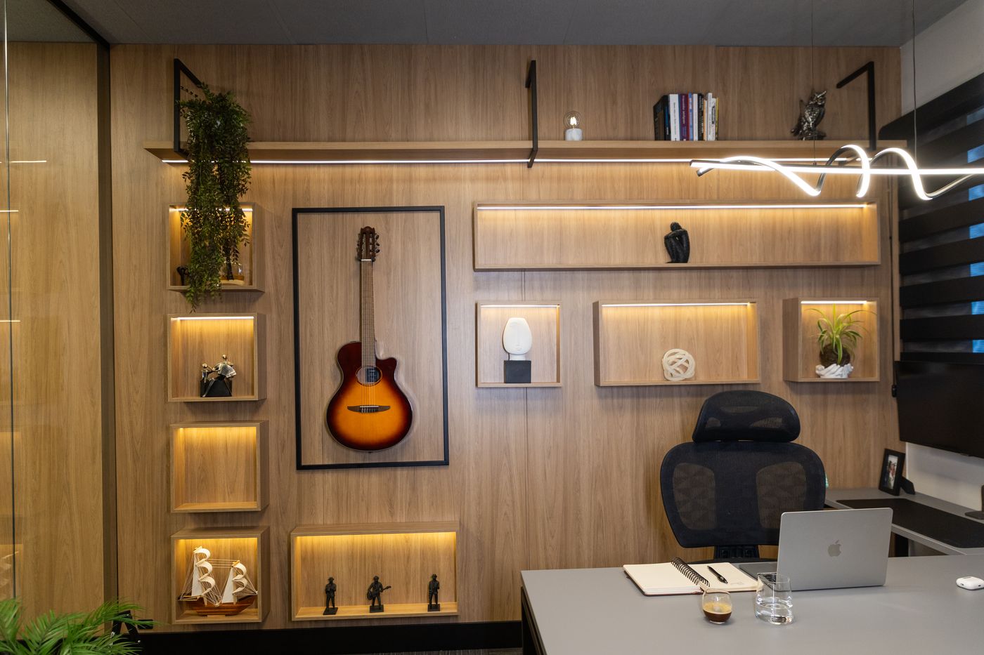 Sala do advogado, com estantes de madeira iluminadas, objetos e o violão na parede