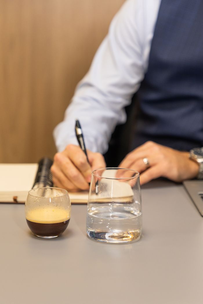 Detalhe de anotações em caderno, com café e água sobre a mesa