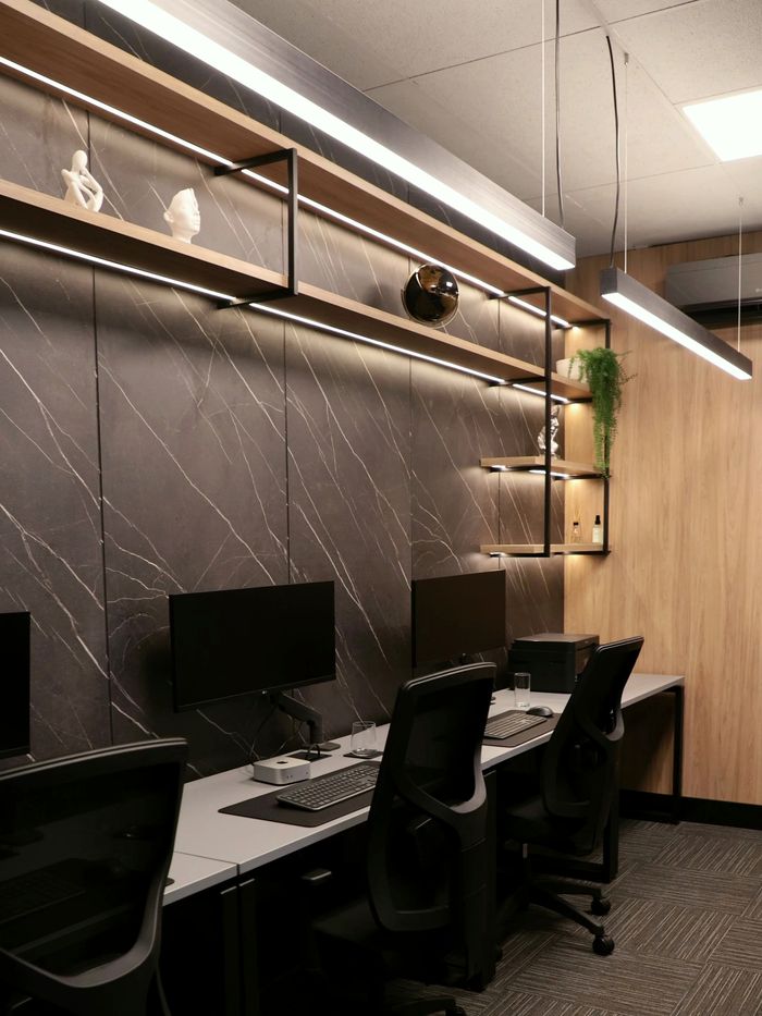Sala da equipe, com estações de trabalho, parede de mármore e prateleiras iluminadas