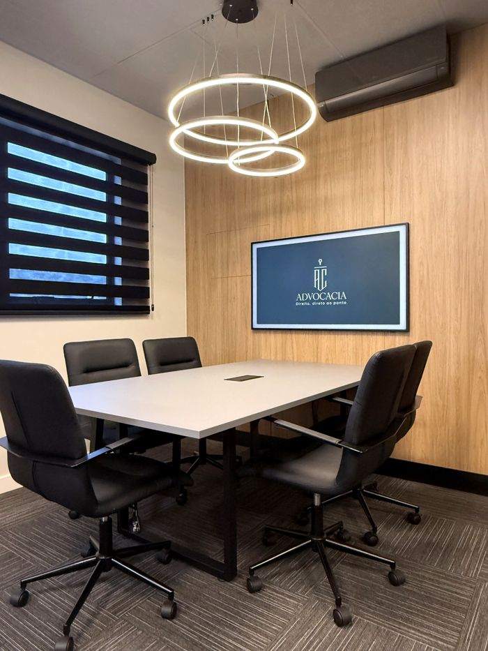Sala de reuniões, com mesa para seis pessoas e a marca do escritório na tela